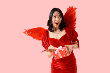 Obraz premium Beautiful young shocked woman dressed as cupid with gift box on pink background. Valentine's Day celebration