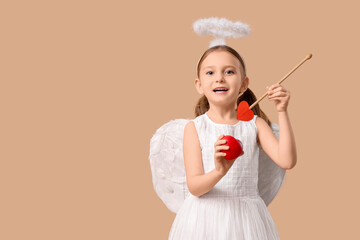 Obraz premium Cute little girl dressed as Cupid with arrow and heart on brown background. Valentine's Day celebration