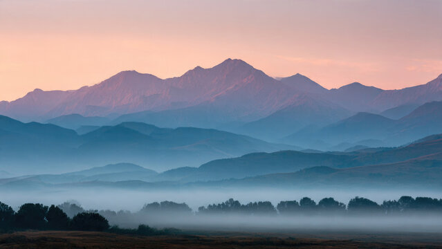Majestic mountain layers rise from a misty valley at dawn, painted with soft pastel hues against a serene, atmospheric sky.