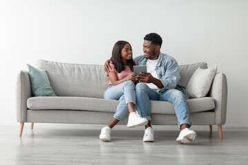 Rest And Relax. Happy loving young African American couple using tab, browsing internet or choosing...