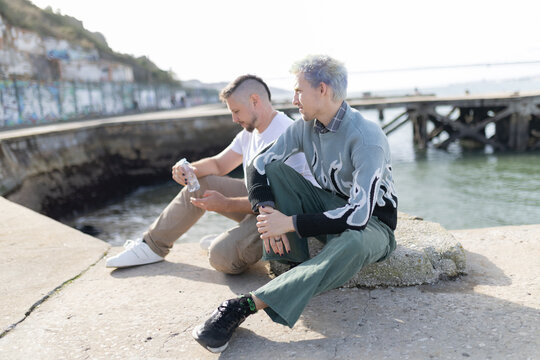 Two men relaxing by water enjoying conversation - Powered by Adobe