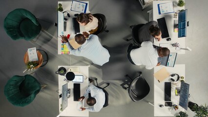 Top down view of manager leads colleagues through business intel and performance metrics. Employees evaluate charts, data and projections to ensure synergy and goals alignment.