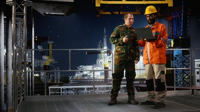 Military officer in camouflage uniform uses walkie talkie on offshore platform, coordinating escort duty, crisis response and coastal defense to safeguard oil rig operations at sea.
