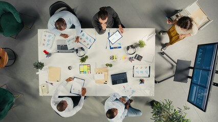 Top down view of employees discussing targets and objectives in a meeting. The corporate work team reviewing files, data and performance metrics for business forecasting.