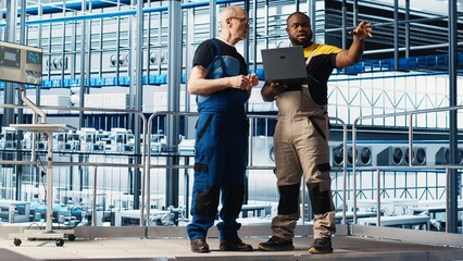Senior engineer talking with intern in smart factory, collecting and analyzing data. Experienced technician helping trainee use tracking software in industrial plant equipped with sensors, camera A