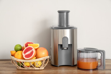 Modern juicer and basket with fresh citrus fruits on table near white wall