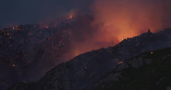 Scary, glowing wild fire smoke rising on large rocky mountain at night