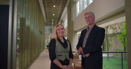 Professional man and woman posing confidently in office corridor, workplace partners standing...
