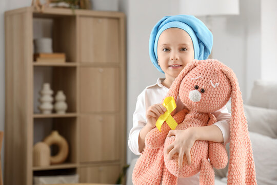 Cute little girl after chemotherapy with yellow ribbon and toy at home. Childhood cancer awareness concept - Powered by Adobe