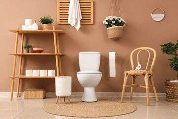 Interior of restroom with toilet bowl, shelf unit and chair