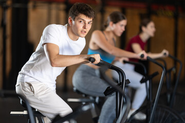 Guy hardly performs exercises on airbike during fitness class. Gym and fitness equipment, visitors...
