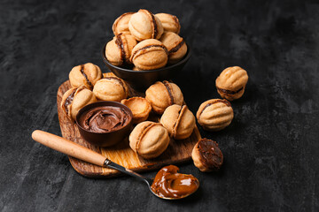 Wooden board and bowl of sweet walnut shaped cookies with boiled condensed milk on black background