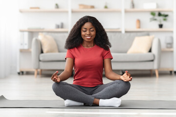 A woman sits cross-legged on a yoga mat, meditating with closed eyes. She enjoys a calm moment in...