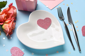 Stylish table setting with gift box and beautiful roses on blue background. Valentine's Day celebration