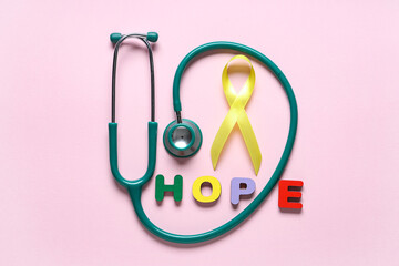 Stethoscope, yellow ribbon and word HOPE on pink background. Childhood cancer awareness concept
