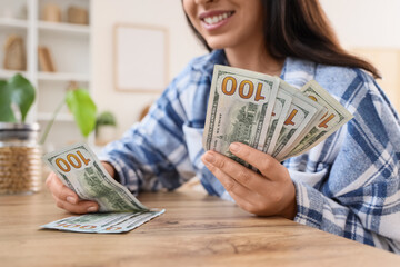 Beautiful woman counting dollar banknotes at table in kitchen, closeup