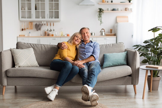 A happy senior couple sits close on a comfortable sofa in a light and airy living room. Warm light fills the space as they smile and share a joyful moment together.