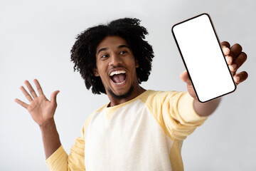 An enthusiastic African American man joyfully presents a smartphone with a blank screen, creating a...
