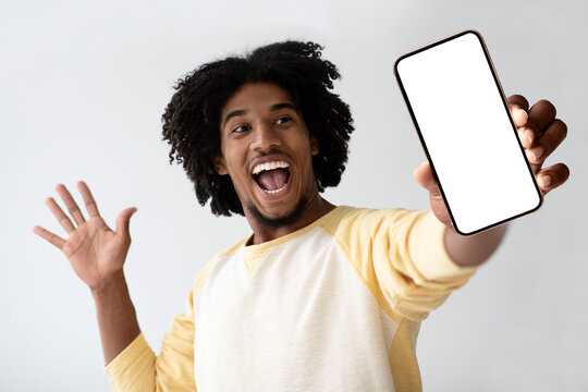 An enthusiastic African American man joyfully presents a smartphone with a blank screen, creating a welcoming space for application or website design.