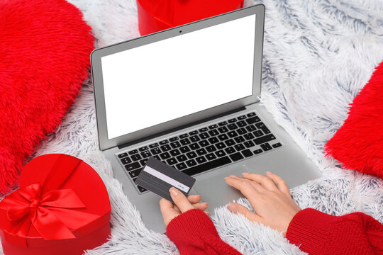 Female hands with credit card, gift boxes and modern laptop on plaid at home. Valentine's Day celebration - Powered by Adobe