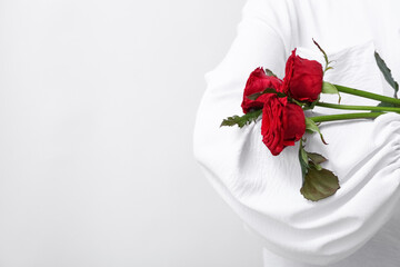 Woman in stylish blouse holding red rose flowers on light background, closeup. Valentine's Day celebration