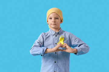 Little boy with childhood cancer awareness ribbon making heart with hands on blue background