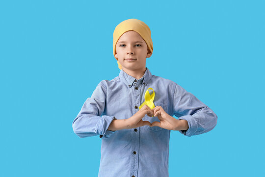 Little boy with childhood cancer awareness ribbon making heart with hands on blue background