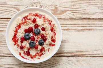 Bowl with tasty oatmeal, syrup and berries on white wooden background