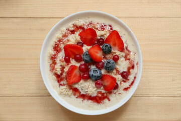 Bowl with tasty oatmeal, syrup and berries on wooden background