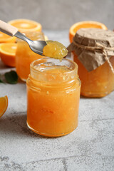 Spoon and jars of sweet orange jam on grey background