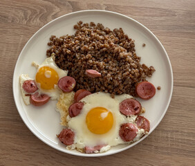 Fried eggs with sausage slices are served with a portion of buckwheat for breakfast