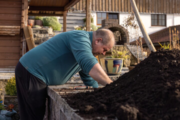 Man doing autumn garden work while preparing soil in a raised bed outdoors