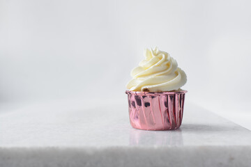 Closeup of a cupcake in pink liners with a vanilla swirl frosting on a white countertop, Pink foil cupcakes with a vanilla buttercream swirl on white background