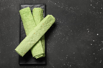 Plate with rolled green lavash on black grunge background