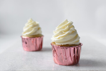 Closeup of a cupcake in pink liners with a vanilla swirl frosting on a white countertop, Pink foil cupcakes with a vanilla buttercream swirl on white background