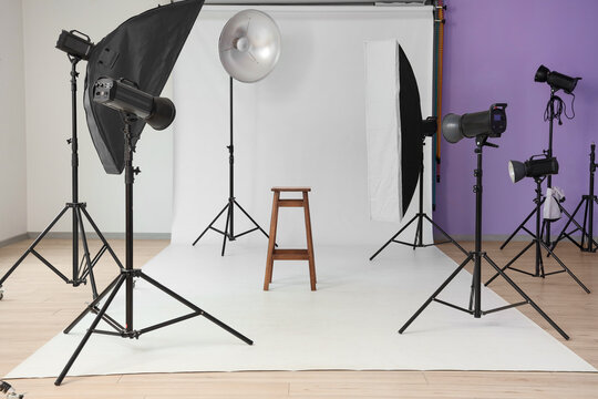 Interior of photo studio with professional equipment, stool and white backdrop - Powered by Adobe