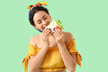 Young African-American woman eating tasty taco on green background