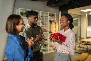 Diverse coworkers celebrating and exchanging gift in office
