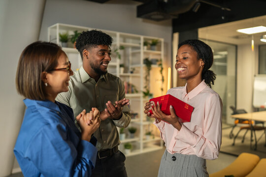 Diverse coworkers celebrating and exchanging gift in office - Powered by Adobe