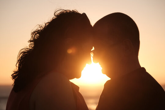 Mature couple touching foreheads in a tender moment at sunset with warm golden light creating a romantic silhouette.