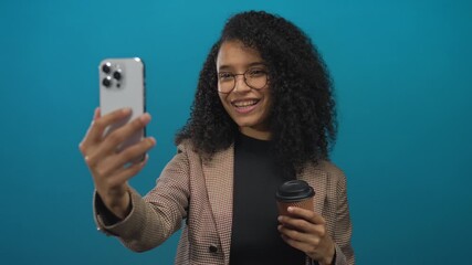 Woman smiling and holding smartphone and coffee cup during studio video call; social connection happiness. - Powered by Adobe