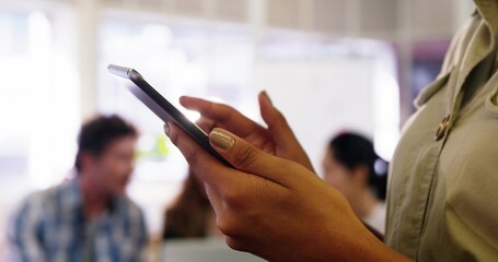 Hands of woman wearing olive blouse tapping phone in open office, with pendant and monitors