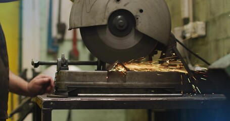 Cutting cutoff saw spinning blade in workshop, sending sparks while workpiece being clamped in vise