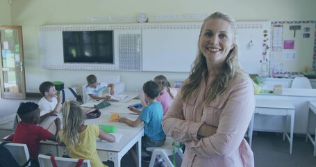 Standing teacher in pink shirt crossing arms watching students using tablet at school, copy space