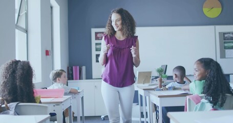 Leading teacher wearing purple blouse and white pants engaging students at desks with whiteboard