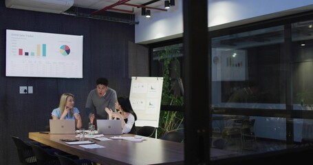Discussing three colleagues presenting charts at office meeting room, in business wear with laptops