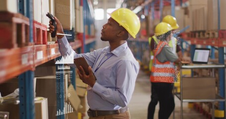 Scanning worker in yellow hard hat and blue shirt in warehouse aisle, using handheld scanner tablet