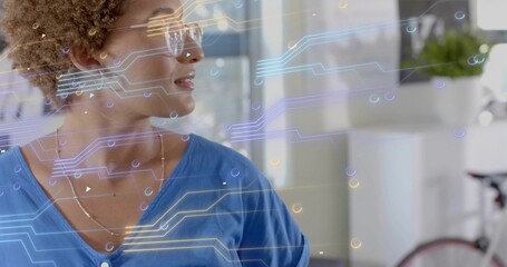 Facing right woman wearing blue V-neck, clear glasses in office with digital overlays and bicycle