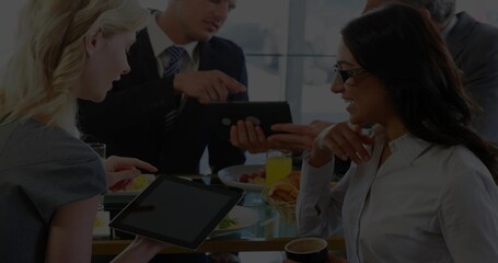 Discussing project, four colleagues in business attire pointing at tablet at office, with breakfast