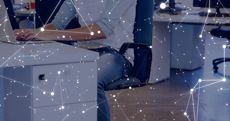 Working adult male typing on laptop at open-plan office in light shirt blue jeans, network overlay